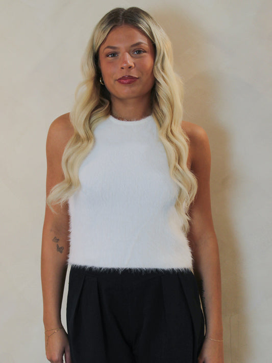 Woman wearing a white fuzzy knit halter style tank styled with black trousers