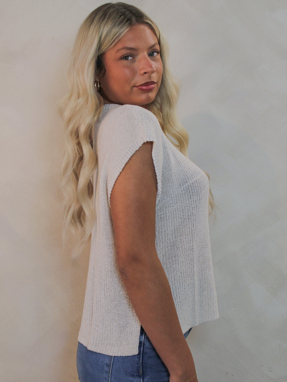 Model wearing a knit  cap sleeve top and blue jeans.