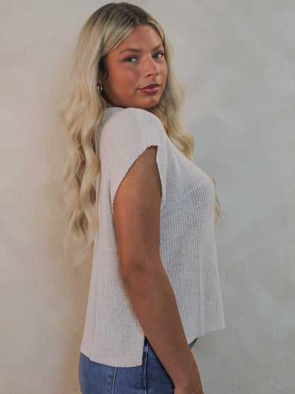 Model wearing a knit  cap sleeve top and blue jeans.