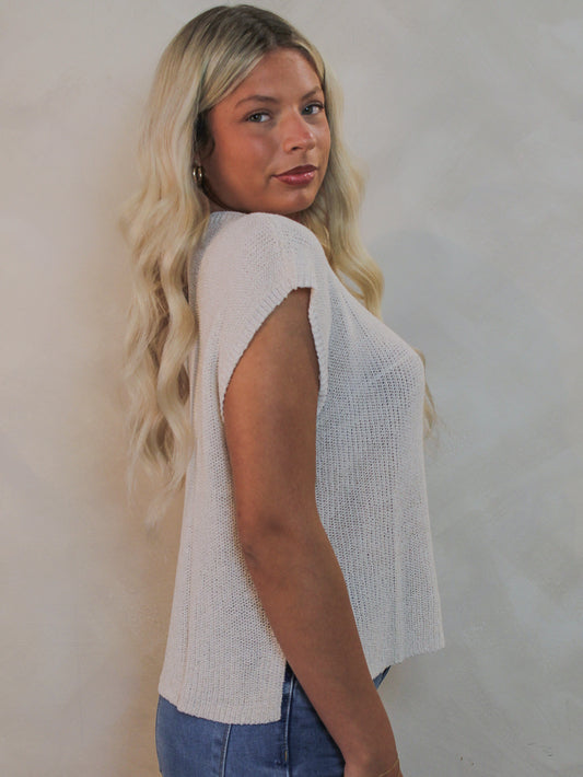 Model wearing a knit  cap sleeve top and blue jeans.