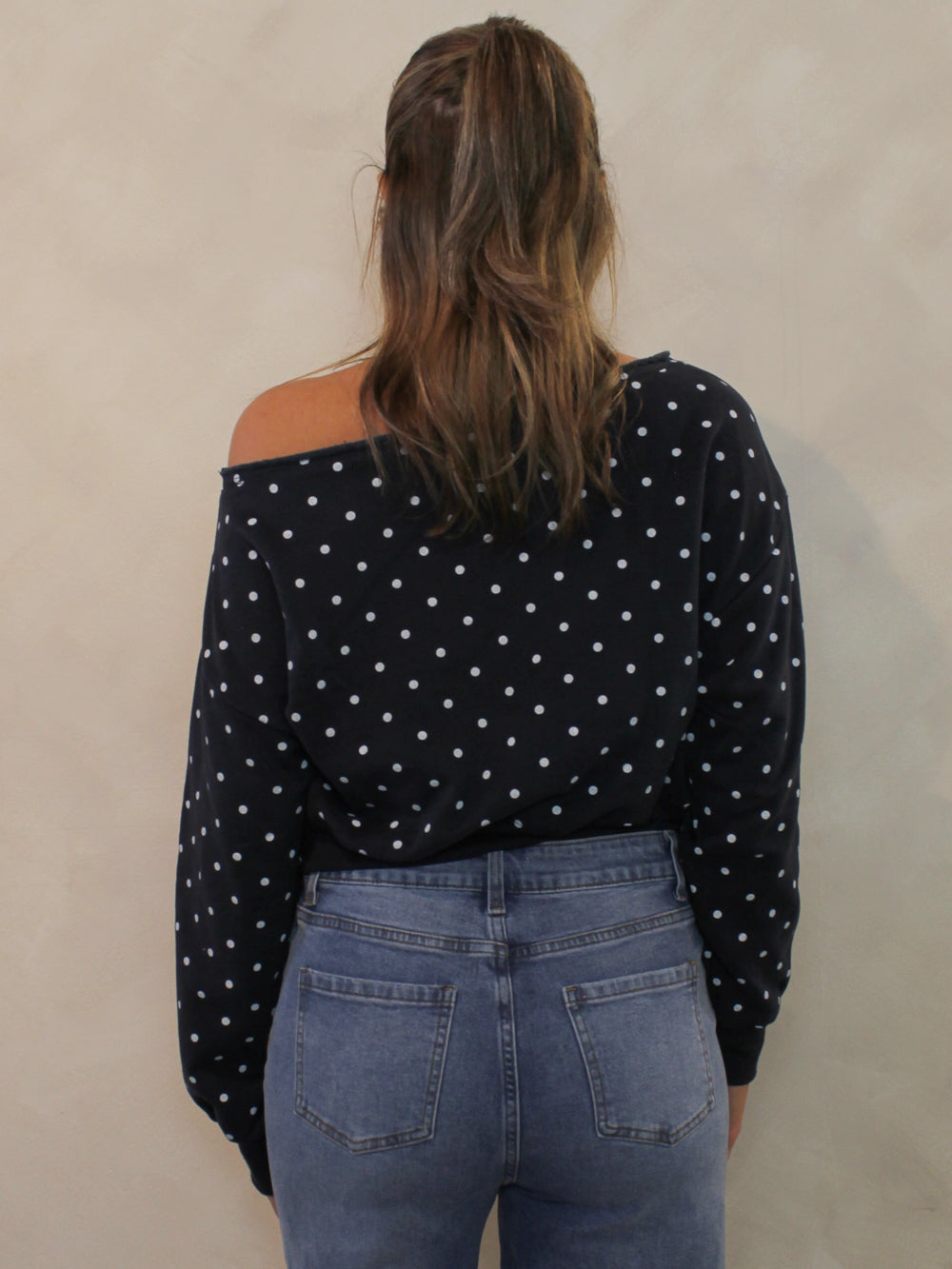 Back view of navy off the shoulder sweatshirt with white polka dots and a cropped hem.