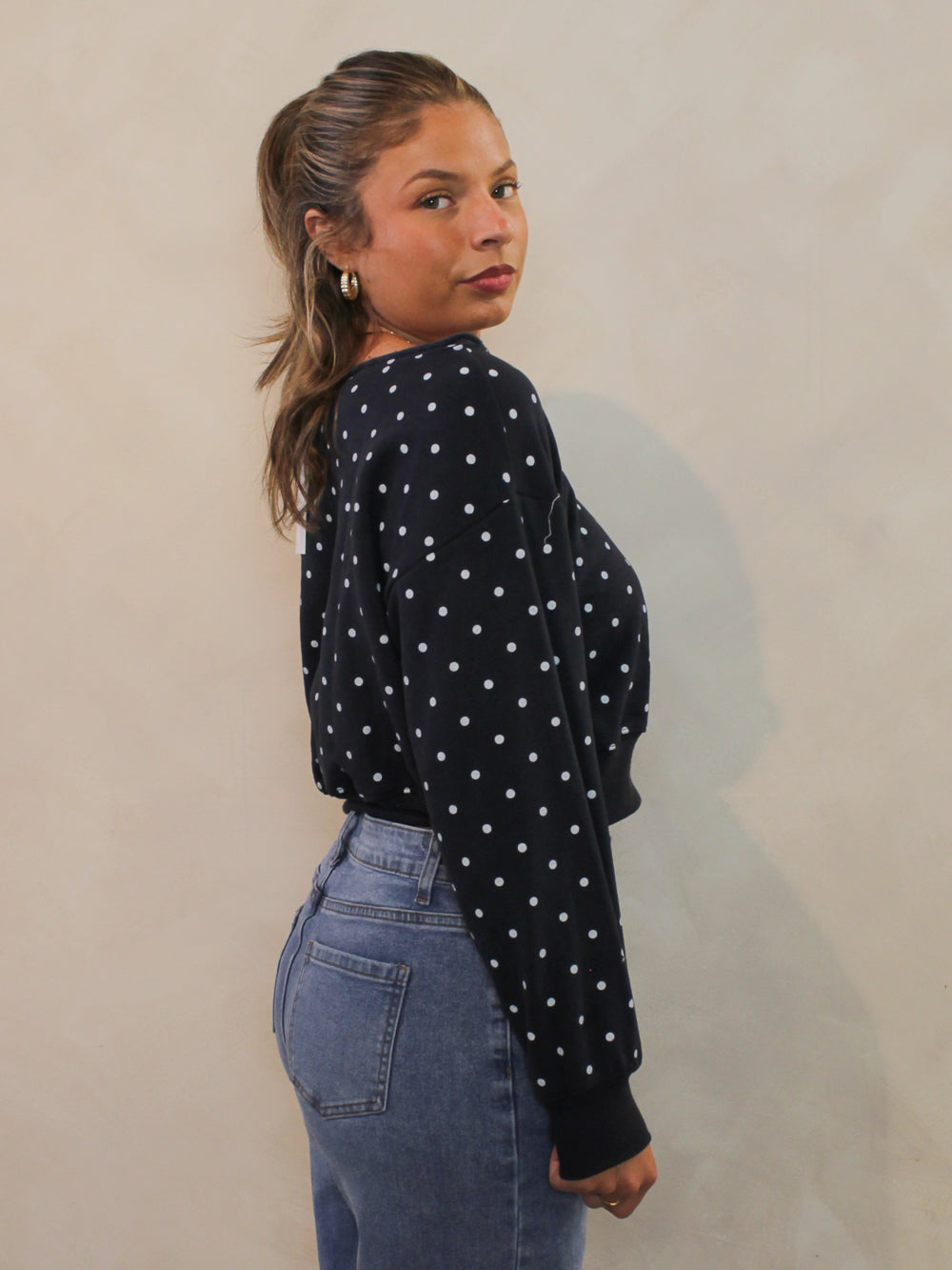 Side view of navy off the shoulder sweatshirt with white polka dots and a cropped hem.