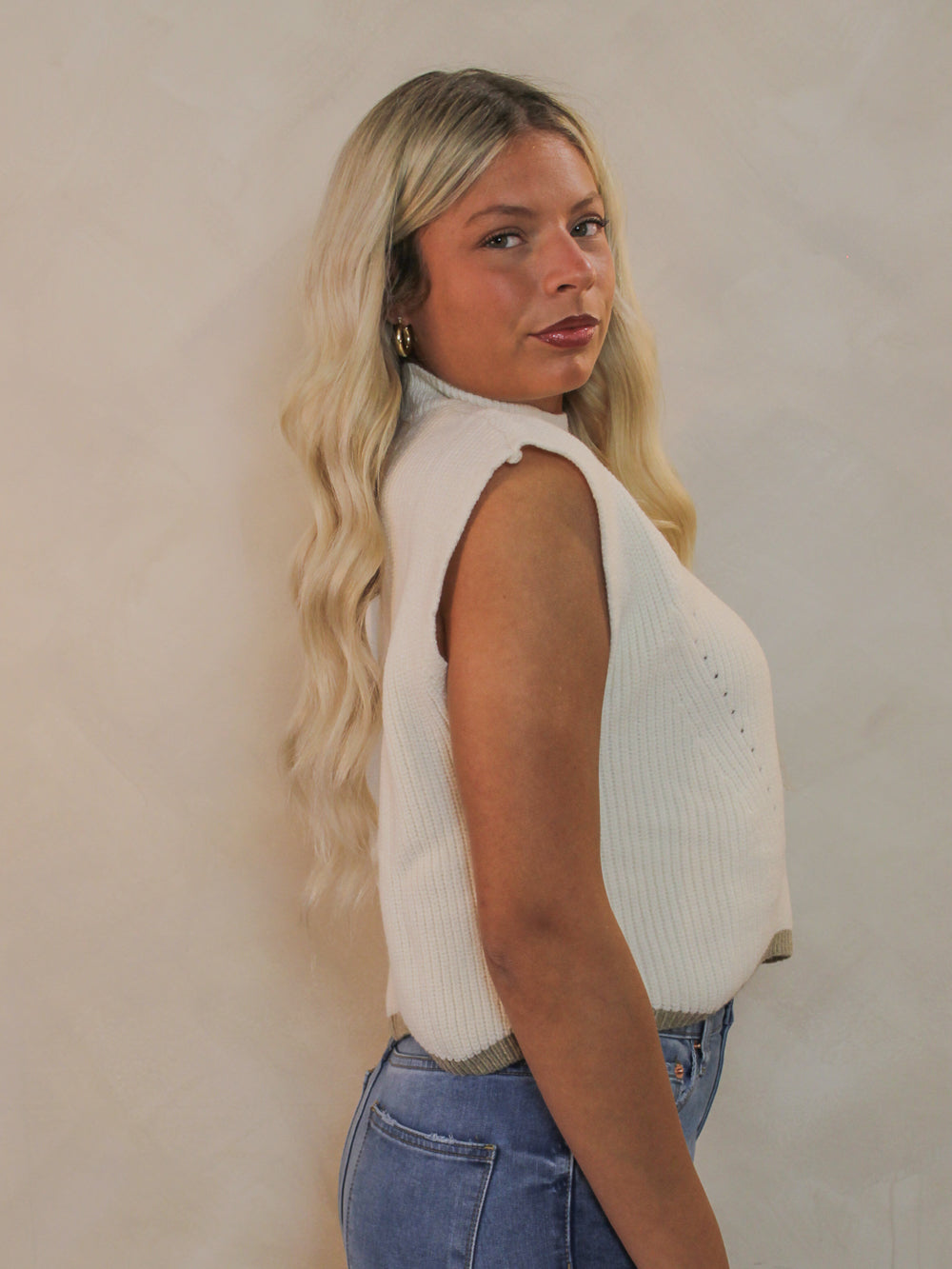 Woman wearing a cream colored sleeveless sweater viewed from the side