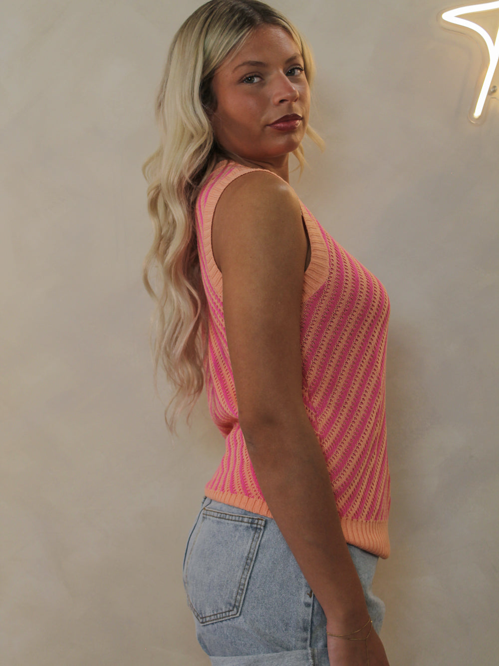 A model wearing a pink and orange striped, sleeveless knit top paired with denim