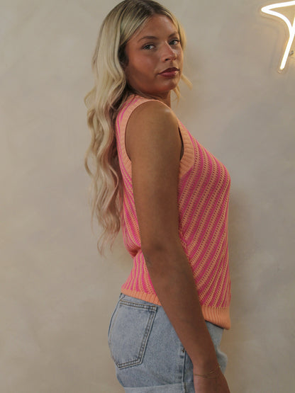 A model wearing a pink and orange striped, sleeveless knit top paired with denim