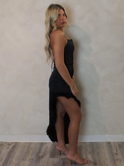 Model wearing a high slit, black satin dress with feather trim and a strappy back