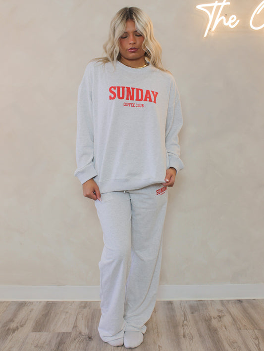 Woman wearing a gray sweatshirt with 'SUNDAY' text in red and matching sweatpants 
