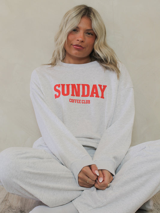 Woman wearing a grey crew neck sweatshirt with the words 'sunday coffee club'