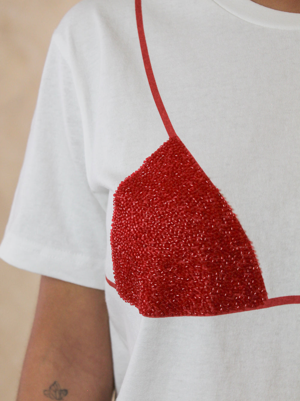 Woman's white tee with a beaded red triangle bikini top graphic