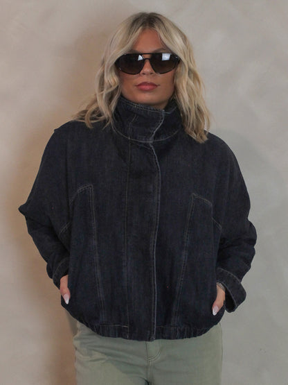 Woman wearing a dark denim, funnel neck jacket with sunglasses and sage green pants