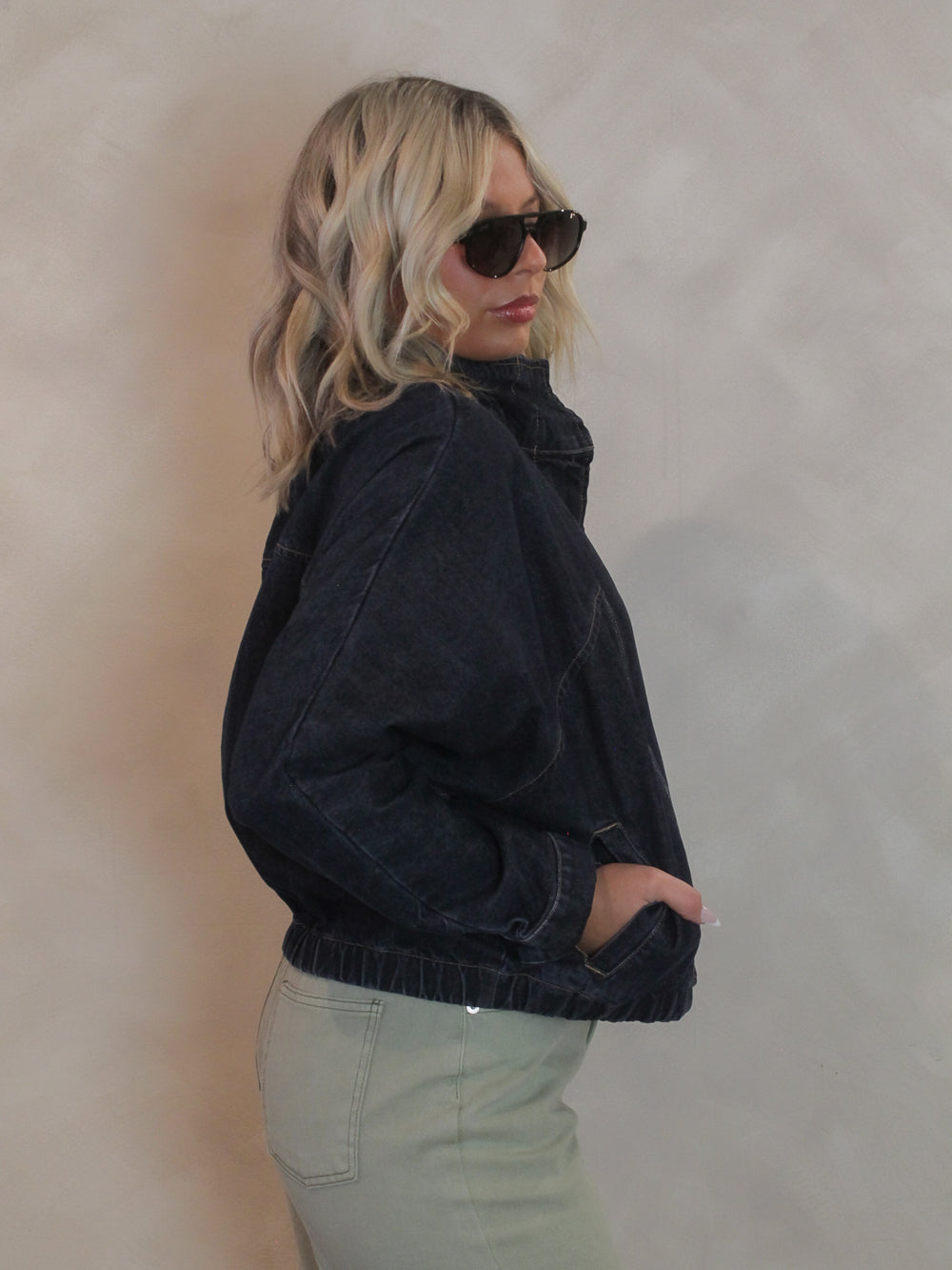 Woman wearing a dark denim jacket with a funnel neckline and elastic hem waist