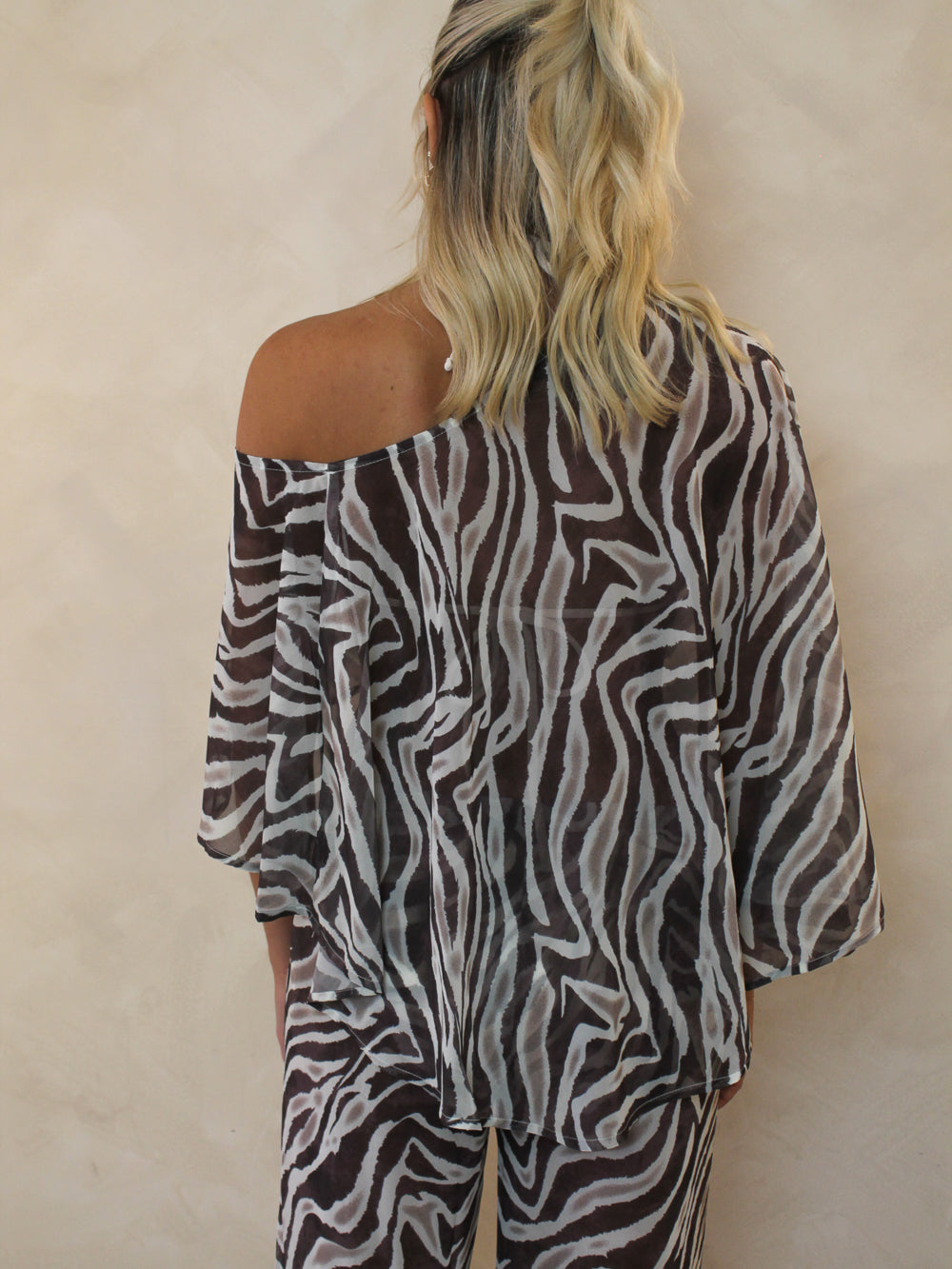 Woman wearing an off the shoulder sheer zebra print cover up.