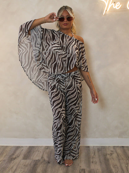Woman wearing a zebra print bathing suit cover up pant set with gold sunglasses