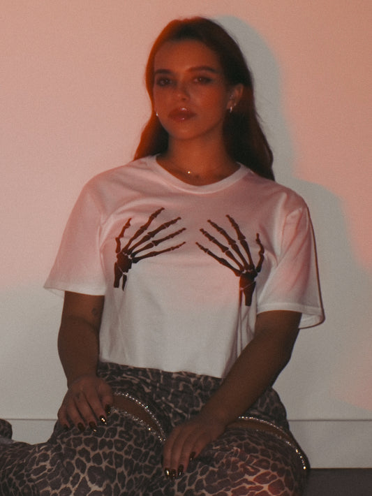 Woman wearing a white cropped tee with black skeleton hands 