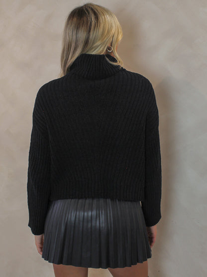 Woman wearing a black knit sweater with black pleated skirt 