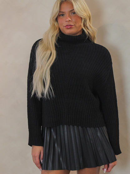 Woman wearing a black turtleneck sweater and black pleated skirt 