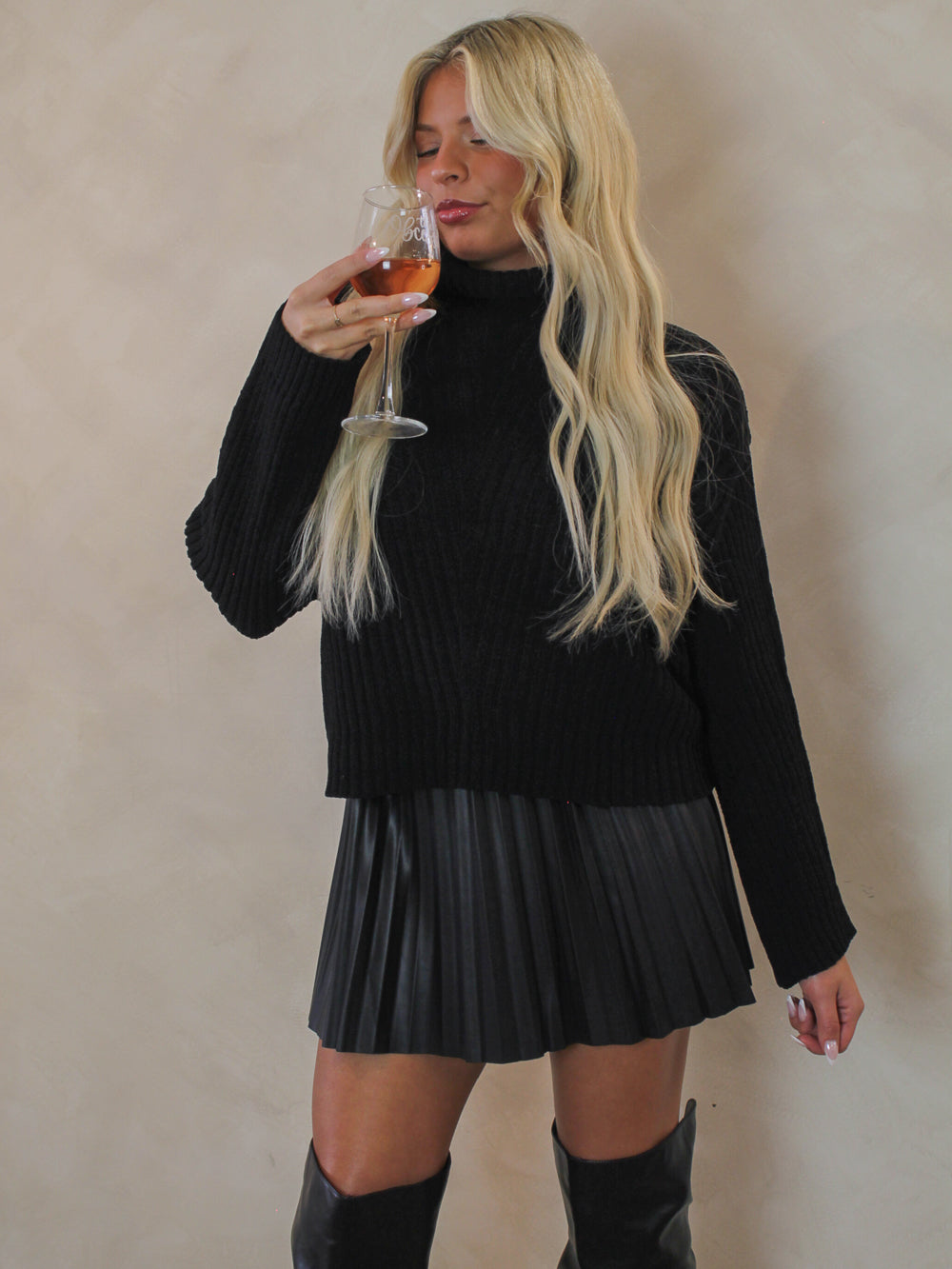 Model wearing a black knit turtle neck and black pleated faux leather skirt for winter