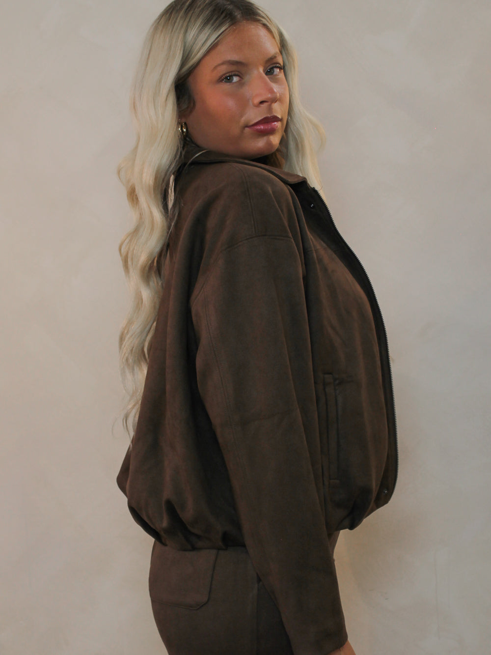 A woman shown from the side wearing a dark brown suede jacket and matching brown pants.