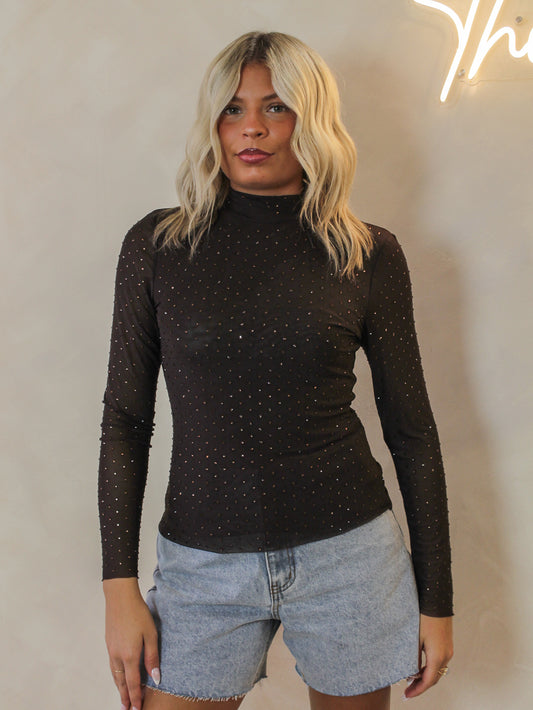 Woman wearing a chocolate brown, long sleeve mesh top with matching sparkling embellishments