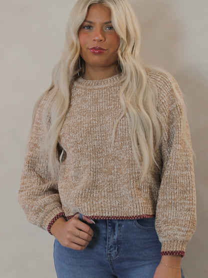 Woman wearing a beige knit sweater with red contrast hem 
