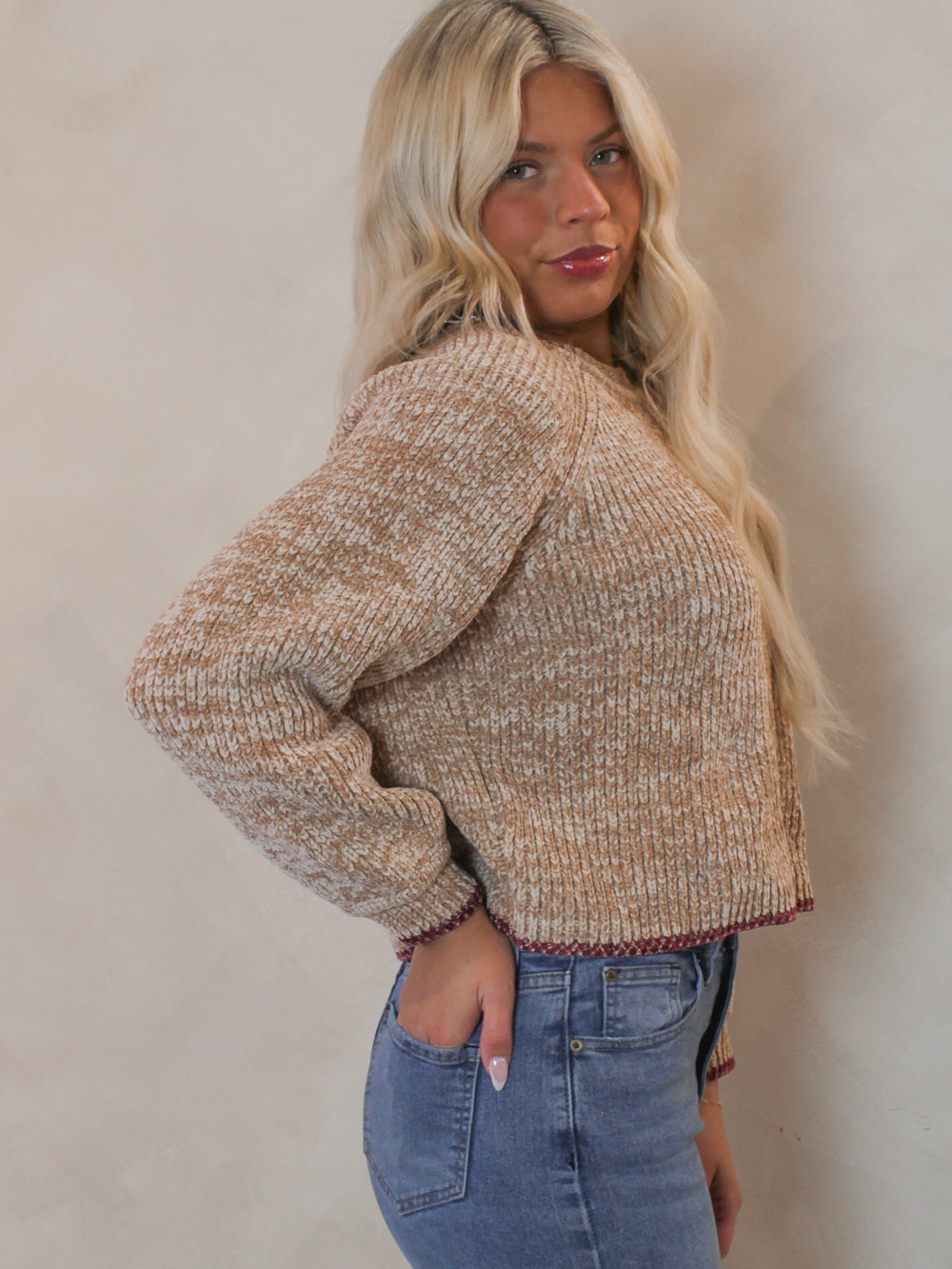 Model wearing a beige knit sweater with red accent hem 