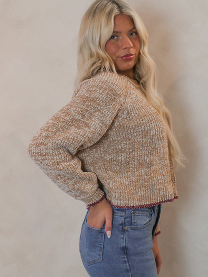 Model wearing a beige knit sweater with red accent hem 