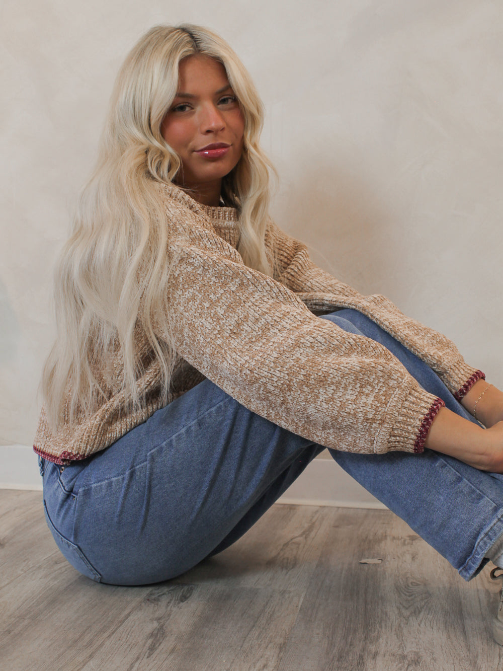 Model wearing a cozy tan sweater with red contrast hem 