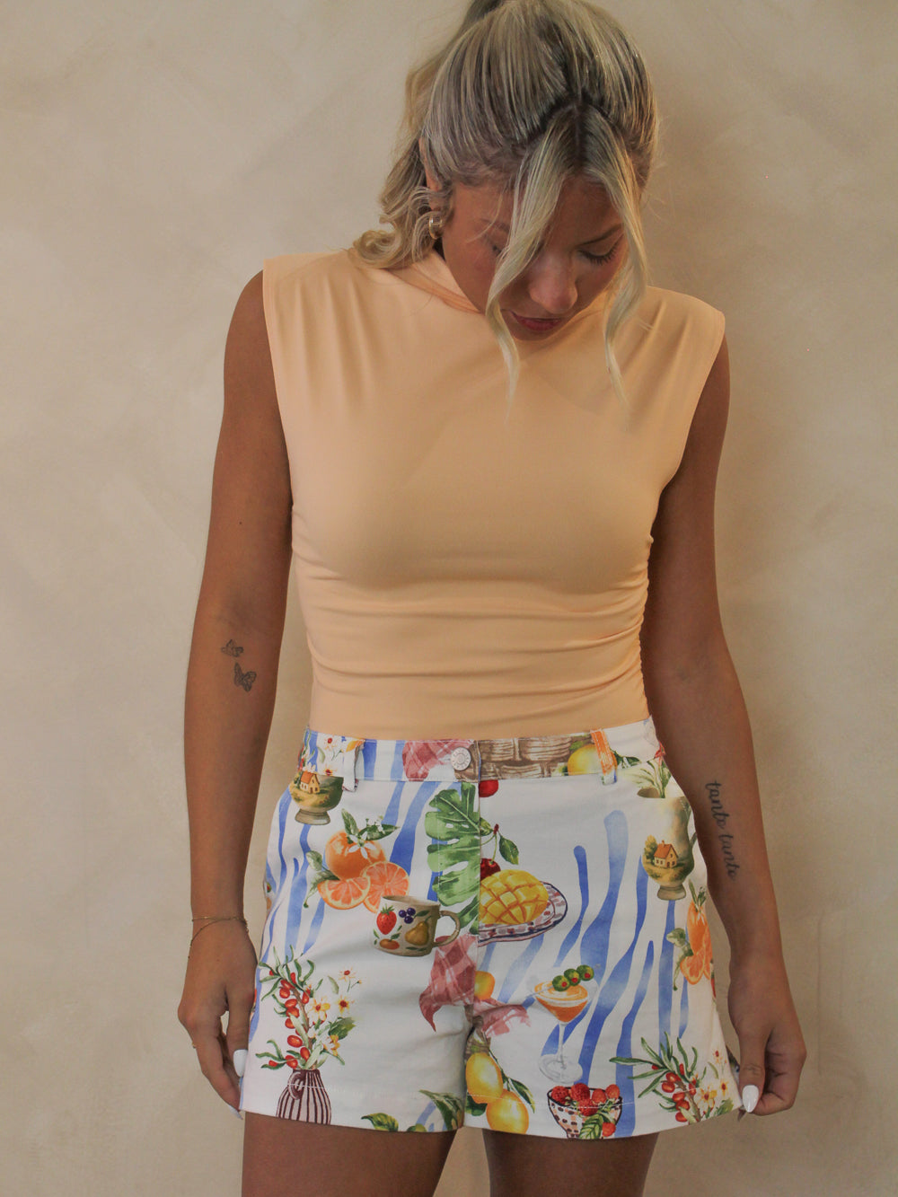 Model wearing fruit print denim shorts styled with a coral mock neck top.