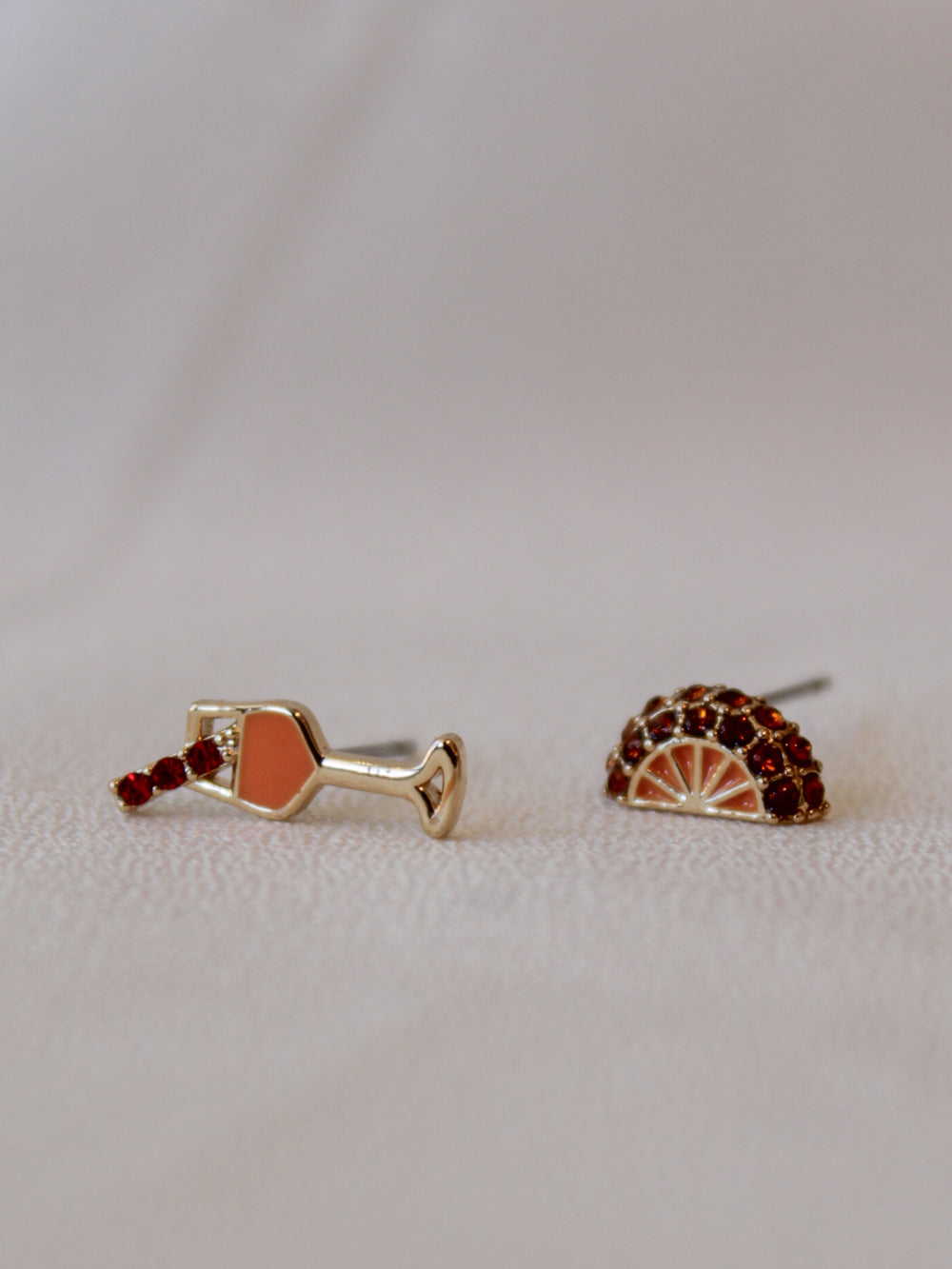 A pair of stud earrings one is a spritz drink and the other an orange slice