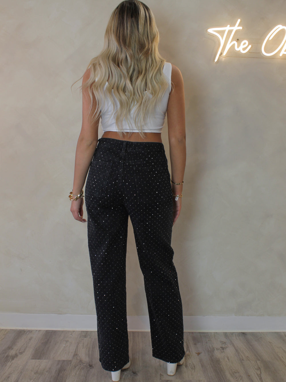 Model wearing a pair of black straight leg jeans with gold rhinestone embellishments 