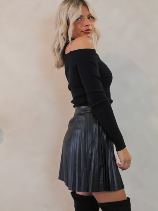 Woman wearing a black off-shoulder top and black, faux leather pleated skirt 