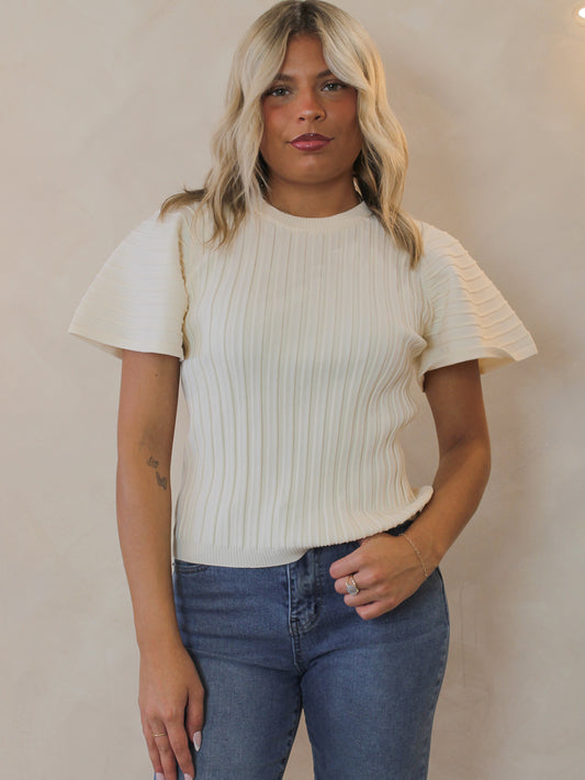 Woman wearing a cream ribbed sweater and blue jeans.