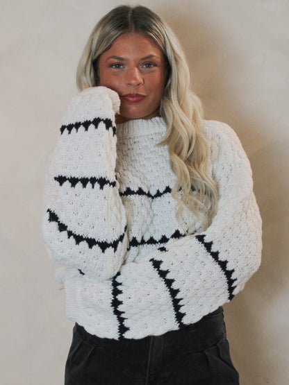 Woman wearing a white knit, oversized sweater with black stripes paired with black shorts.