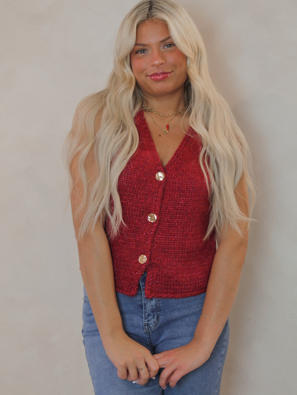 Model wearing a red sleeveless sweater with gold buttons 