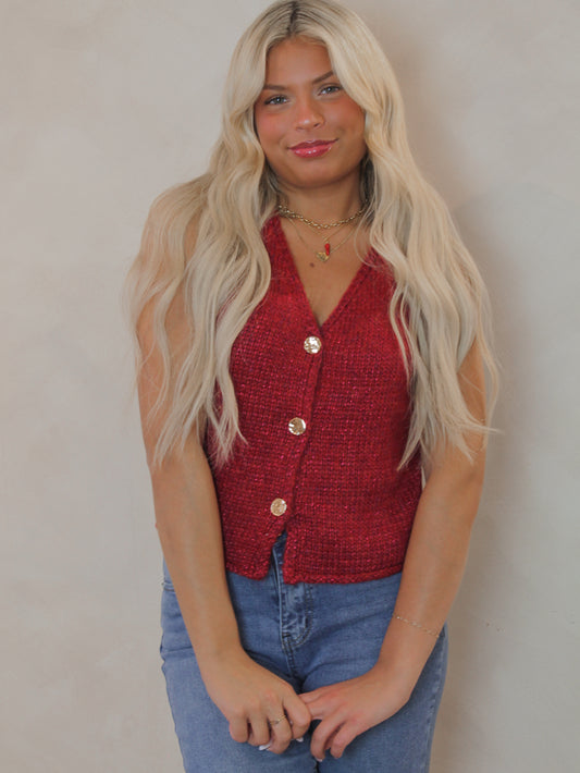 Model wearing a red sleeveless sweater with gold buttons 