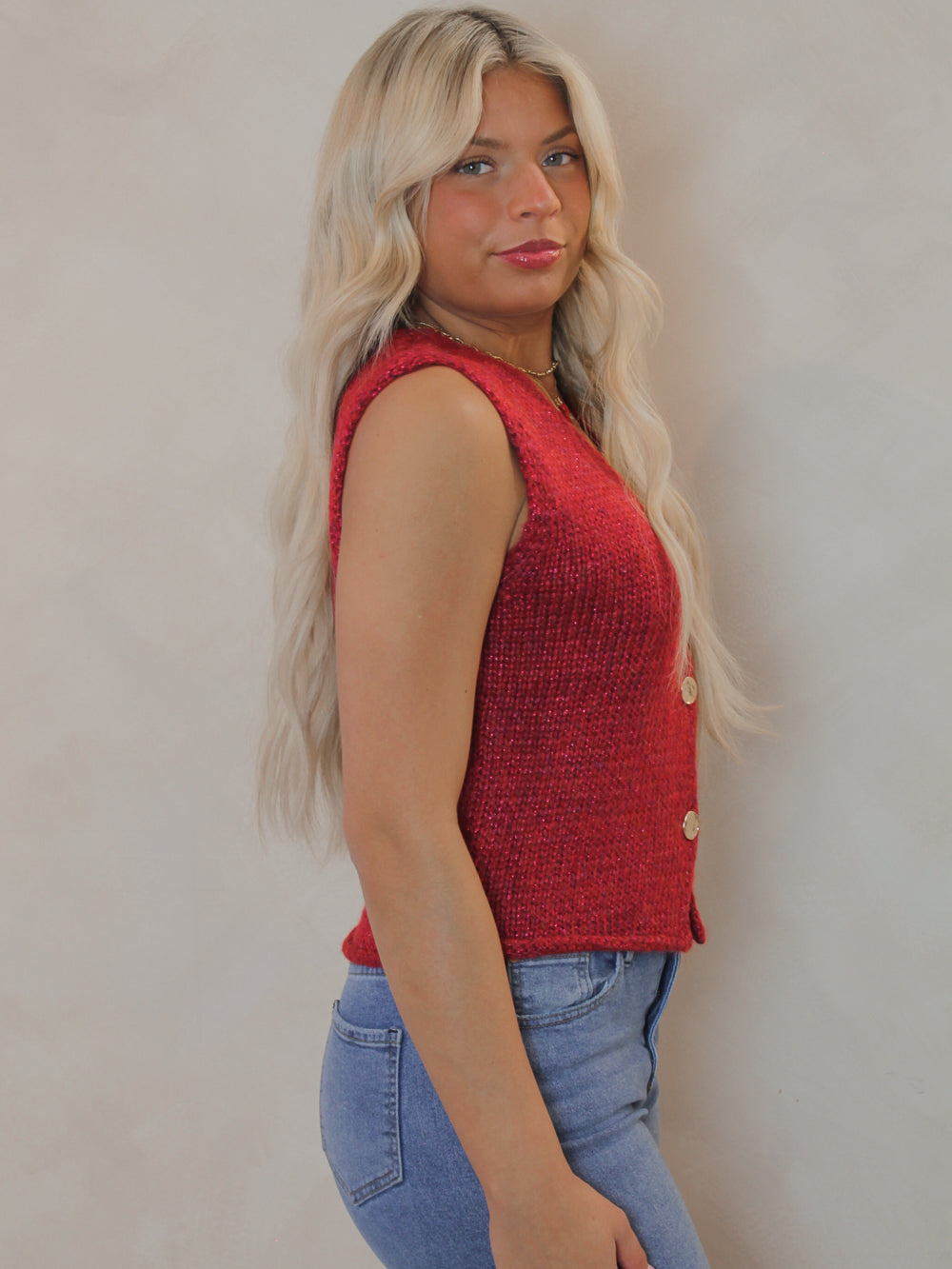 Woman wearing a red sleeveless sweater with gold hammered buttons 
