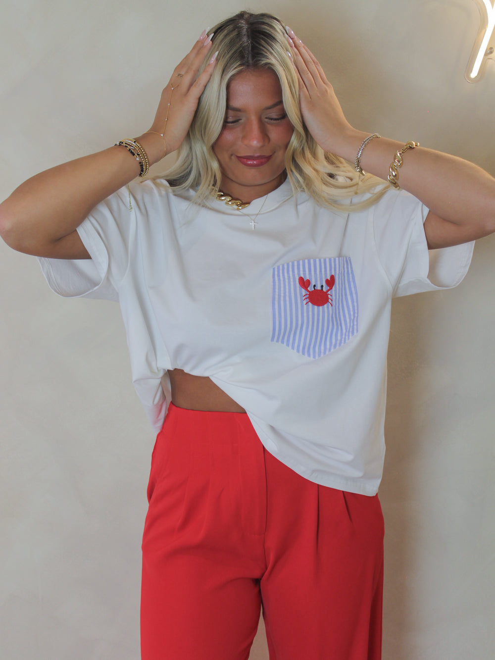 Woman wearing a white oversized shirt with a striped pocket design with an embroidered crab, paired with red pants 