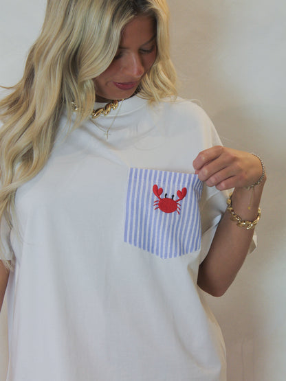 Model wearing a white tee with a striped front pocket and embroidered crab