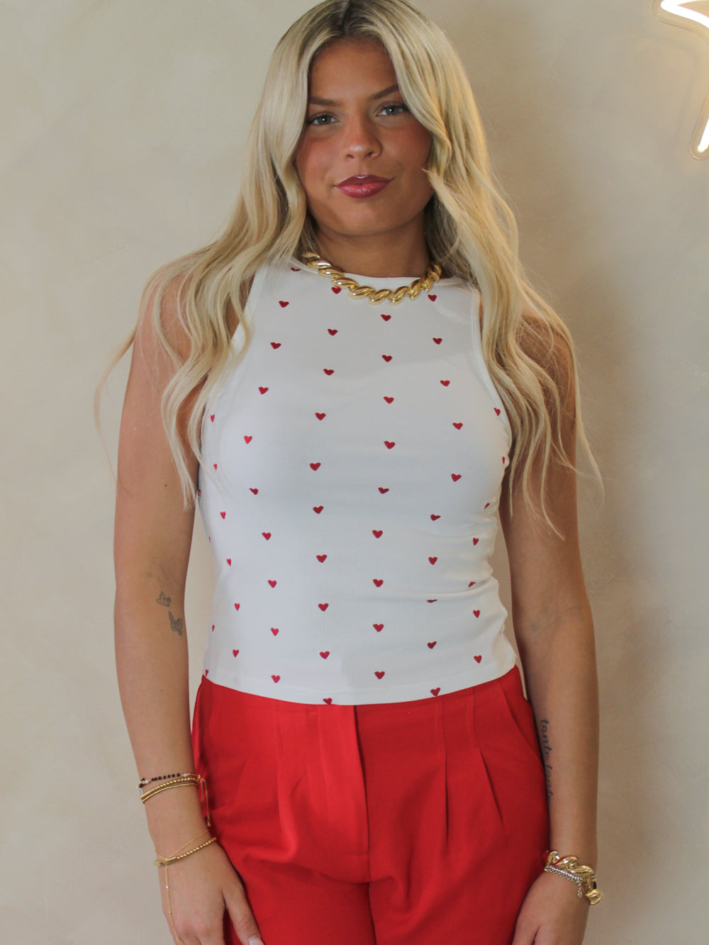 Model wearing a white tank with hearts all over and red pants 