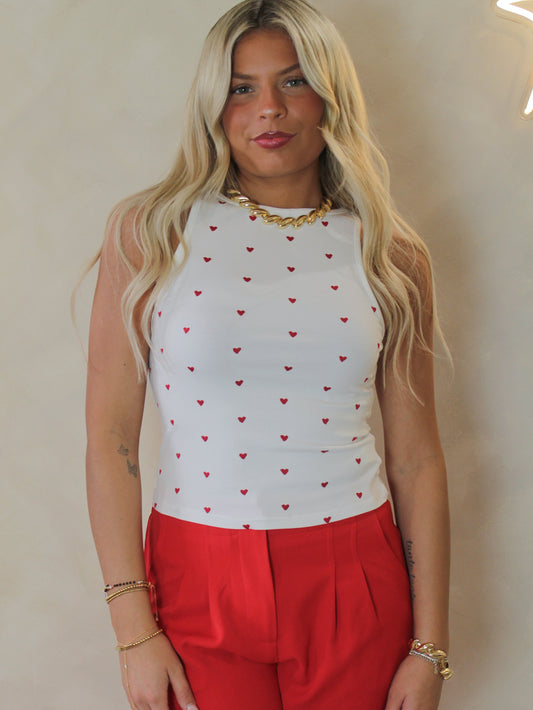 Model wearing a white tank with hearts all over and red pants 