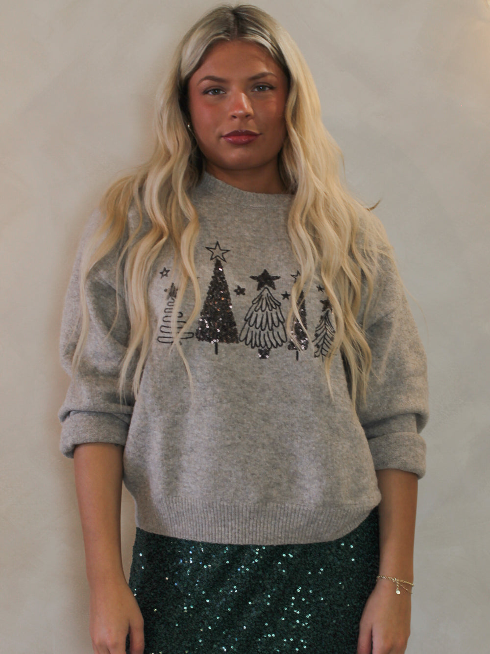 Model wearing a cozy grey sweater with sequin Christmas trees