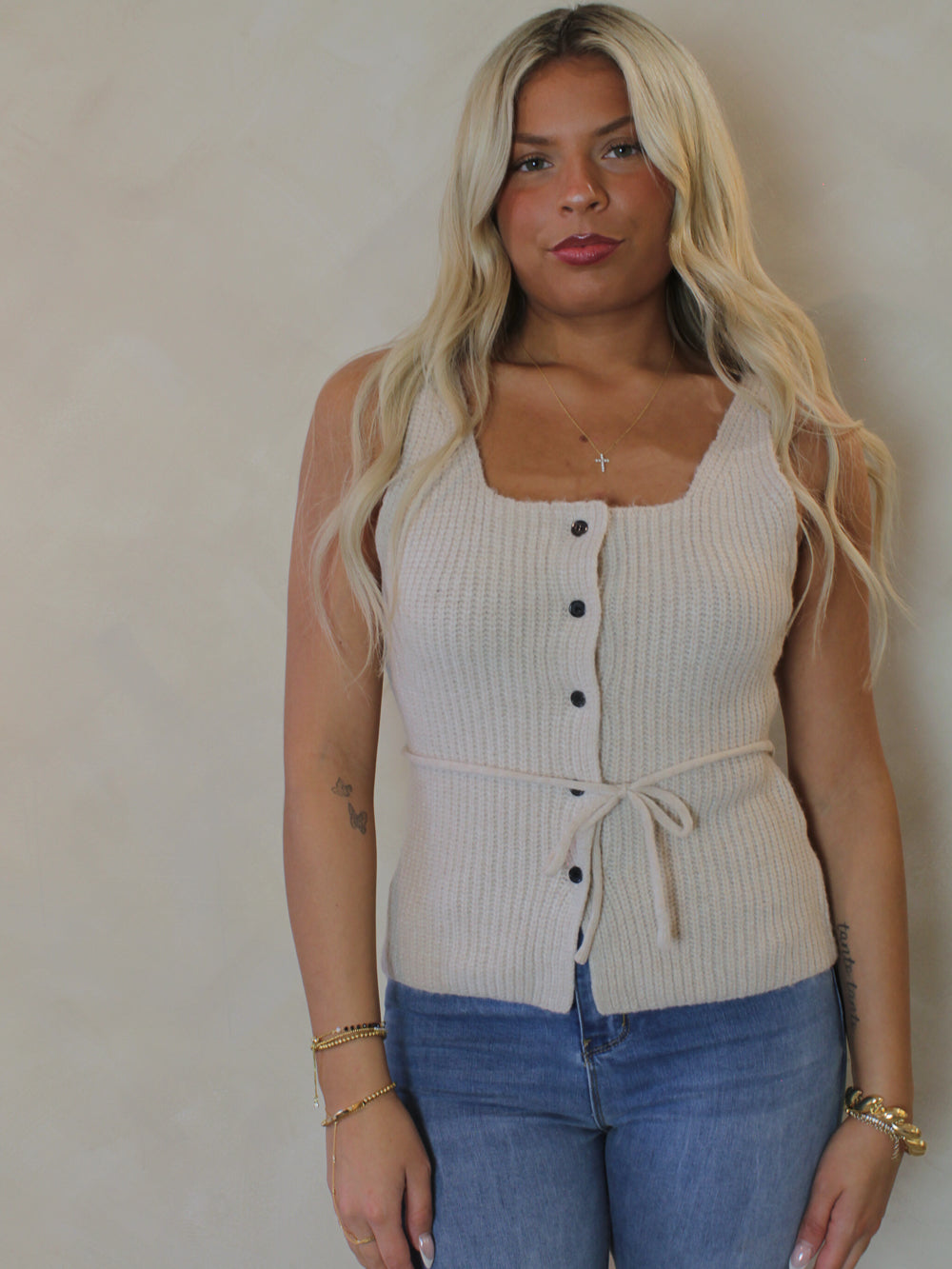Model wearing a beige ribbed knit tank top with buttons and blue jeans a