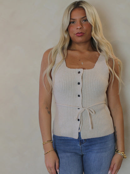 Model wearing a beige ribbed knit tank top with buttons and blue jeans a