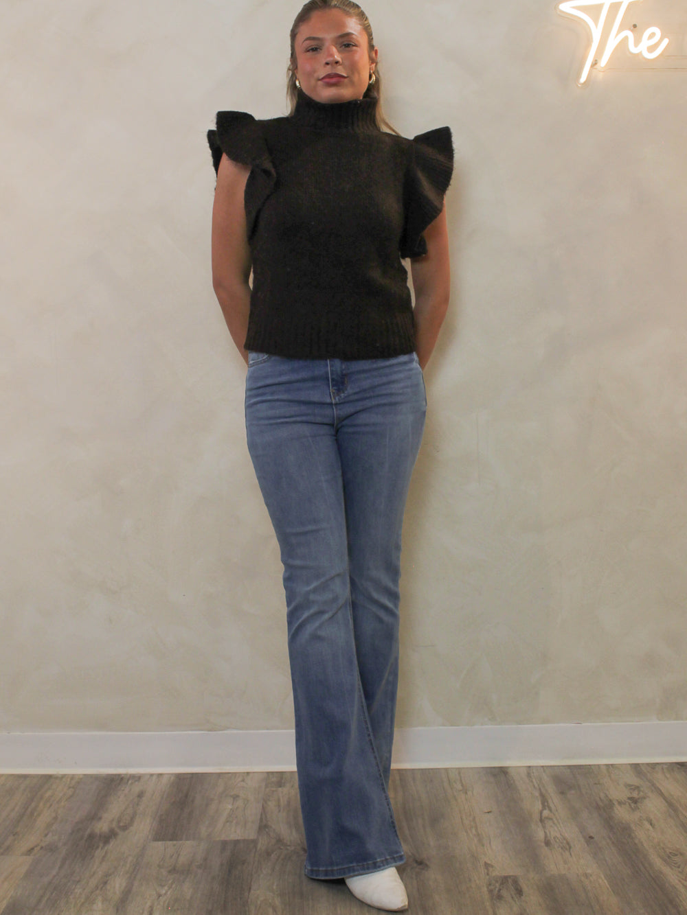 Dark brown ribbed sweater with a mock neck and dramatic ruffle cap sleeves styled with light blue flare jeans.