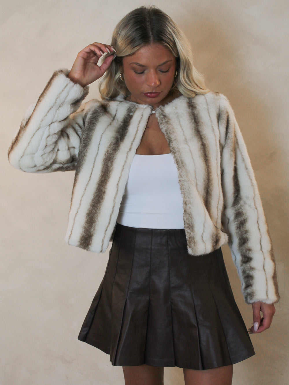 Woman wearing a brown and white faux fur jacket styled with a brown leather skirt