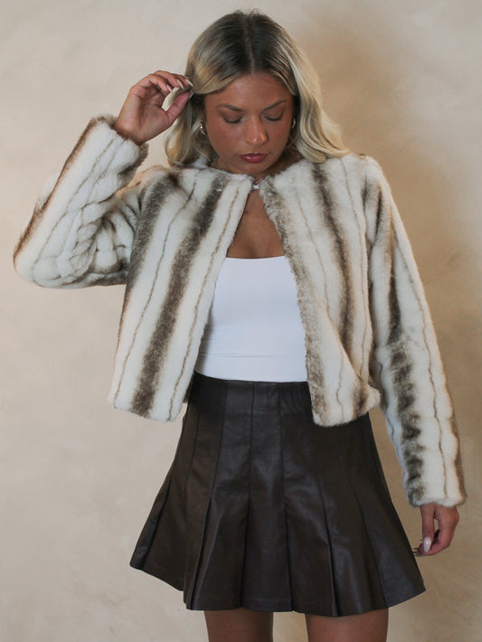Woman wearing a brown and white faux fur jacket styled with a brown leather skirt