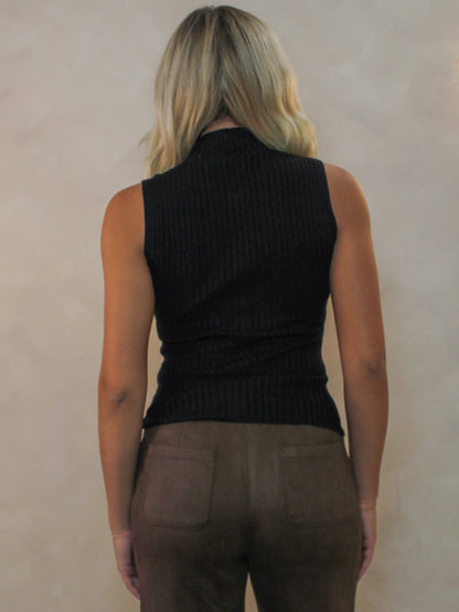 Model viewed from behind wearing a sleeveless black ribbed mock neck top and brown pants.