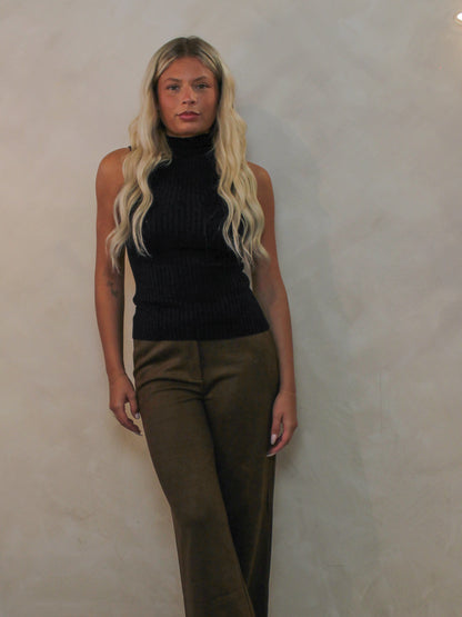 Model wearing a sleeveless black ribbed turtleneck top styled with brown wide-leg pants.