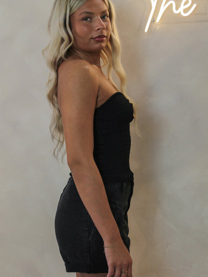 Model wearing a black strapless tube top and a black pair of shorts.