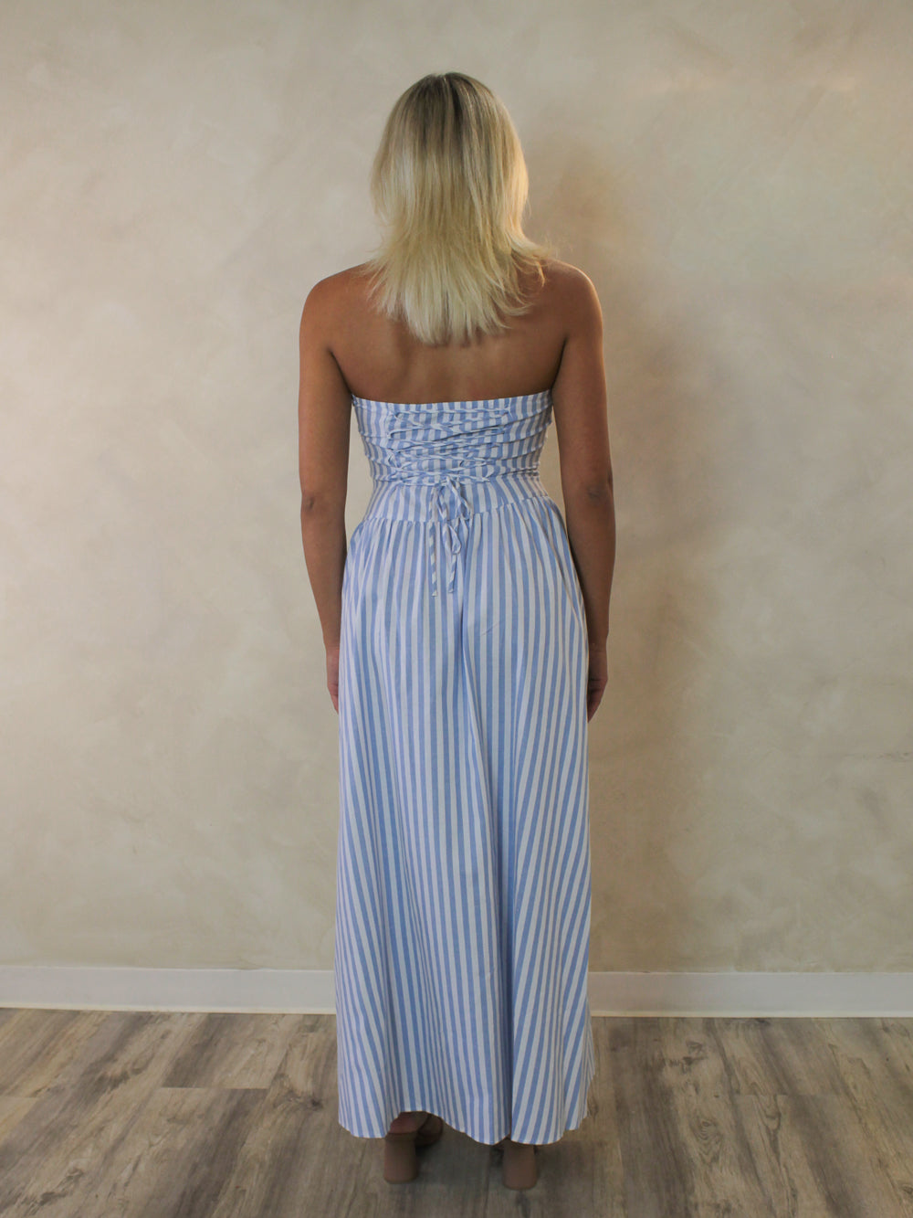 the back view of a blue and white striped maxi dress with a lace up corset detail.
